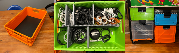 an assortment of my sidio crates. On the left, an empty half height orange v1 crate. In the middle, an overhead view of a green half-height crate with a series of dividers and an assortment of cables. On the right, a series of crates nestled underneath my pinball machine