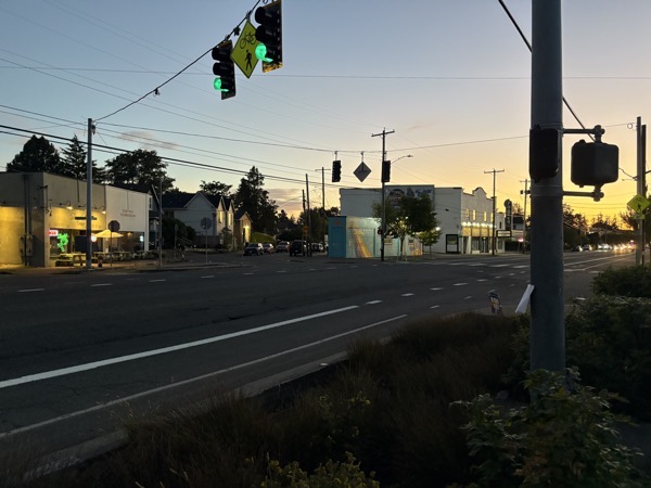 a sunset shot of a particular intersection of a road in my neighborhood. There's a colorful former weed store in the center of the image across the street.
